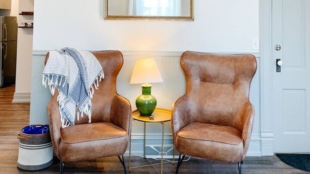 A room with two brown leather chairs, a green lamp, a small table, a chandelier, and a mirror on the wall. - South Shore Condo @ Bayfield Guest House (Bayfield)