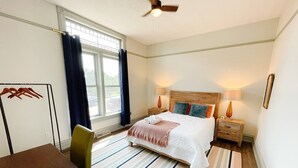 A hotel room with a bed, bedside tables, a chair, a desk, and a window with curtains. - South Shore Condo @ Bayfield Guest House (Bayfield)