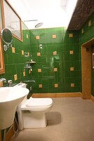 Un baño con paredes de azulejos verdes, un lavamanos blanco y un inodoro.