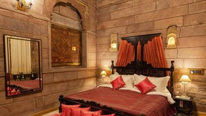 A traditional room with a large bed, ornate wall sconces, and a patterned rug.