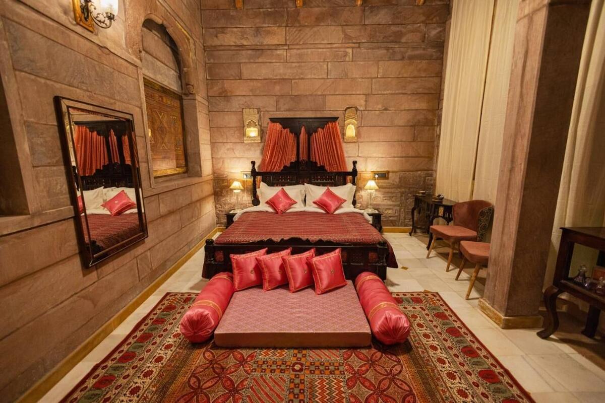 A bedroom with a large bed, a mirror, a fireplace, and a carpet.