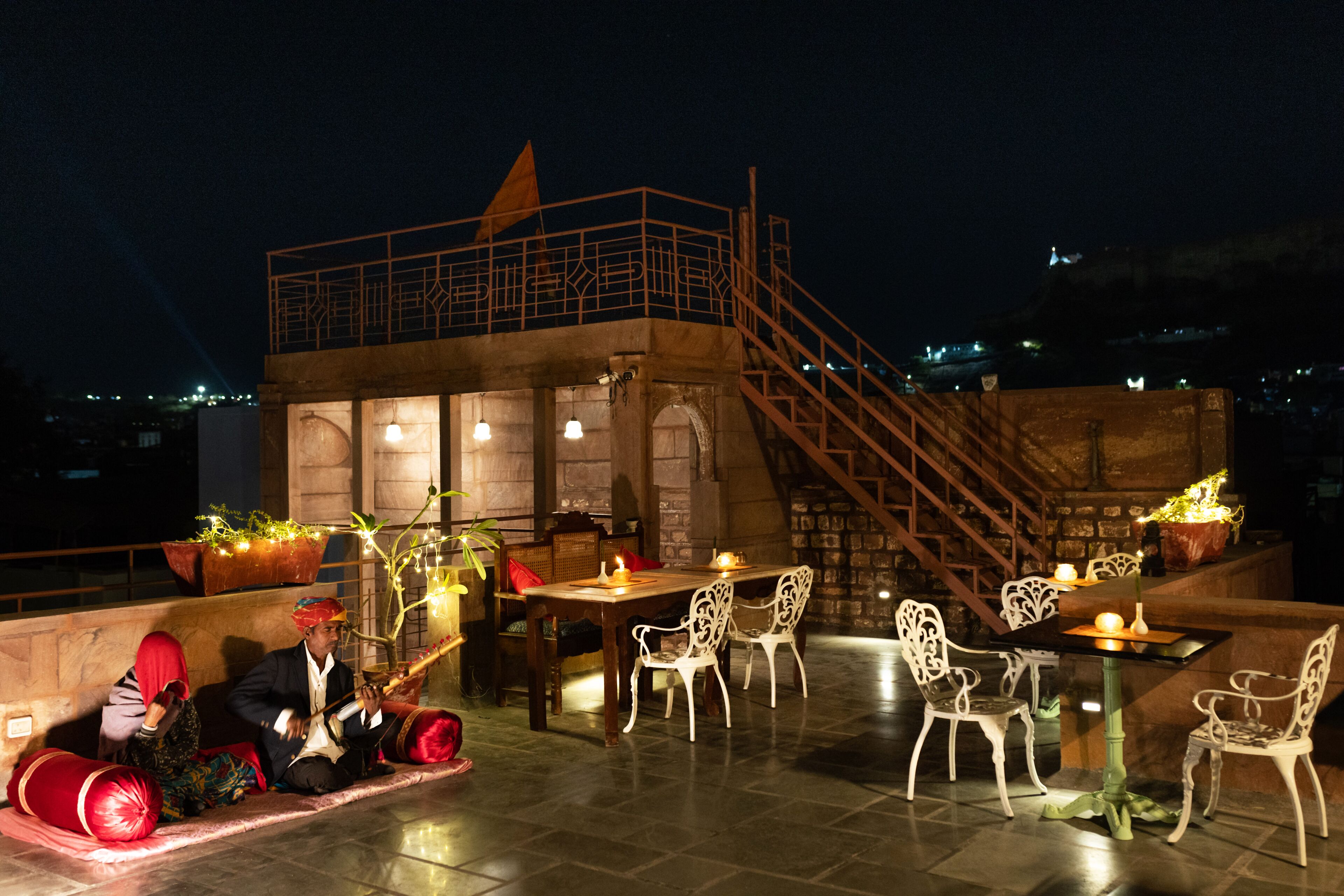 An outdoor dining area with a terrace, stone walls, and a staircase leading to an upper level.
