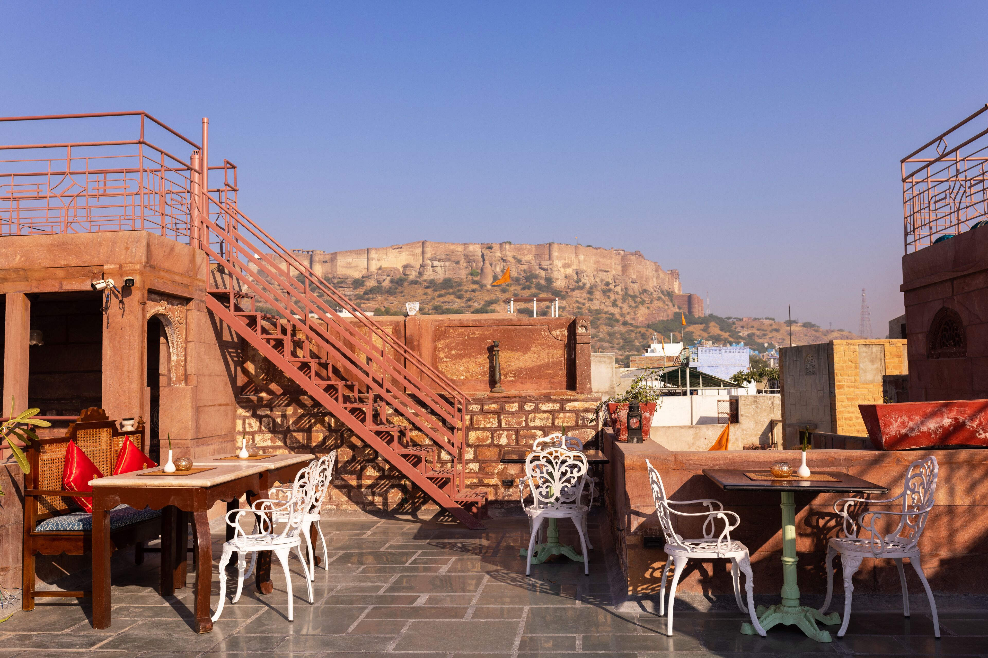 A terrace with outdoor seating, a staircase, and a view of a historic fort in the background.