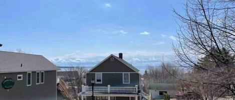 Ein zweistöckiges Haus mit Veranda und kleinem Balkon, umgeben von Bäumen und blauem Himmel.