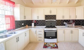 A kitchen with white cabinets, a black tiled backsplash, a stove, and a microwave.