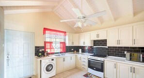 A kitchen with a washing machine, oven, microwave, and a ceiling fan.