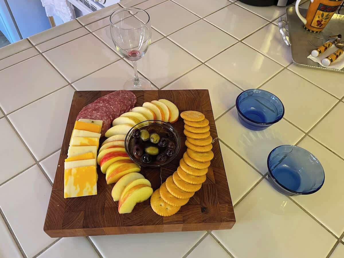 A charcuterie board with cheese, cured meats, apples, olives, and crackers on a wooden board.