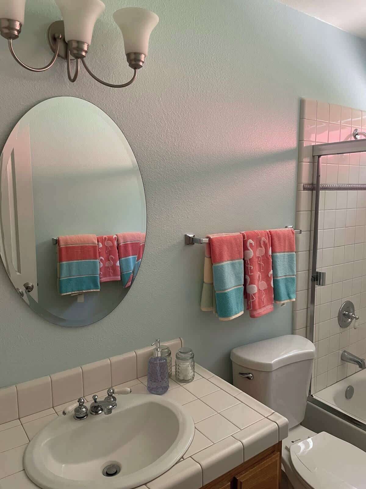 Une salle de bain avec un miroir rond, deux porte-serviettes avec des serviettes à rayures, un lavabo avec un robinet et des toilettes.