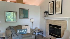 A living room with a sofa, armchair, fireplace, and framed artwork on the wall. - Auburn Party of 8 (Auburn)