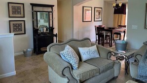 A living room with a sofa, a coffee table, and a dining area in the background. - Auburn Party of 8 (Auburn)