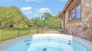 A hot tub with a stone exterior wall and a view of a green lawn and trees.