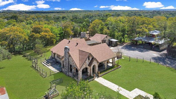 A stone building with a red roof, surrounded by a well-maintained lawn and a fence.