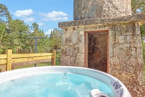 A stone structure with a door, a wooden fence, and a hot tub. - Milk Bath Springs | Pet-Friendly Historic Downtown Cottage (Dripping Springs)