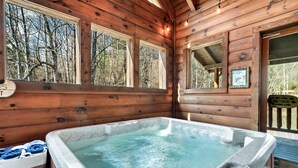 Interior de una cabaña de madera con jacuzzi, ventanas amplias y un cartel que indica una zona de pesca.