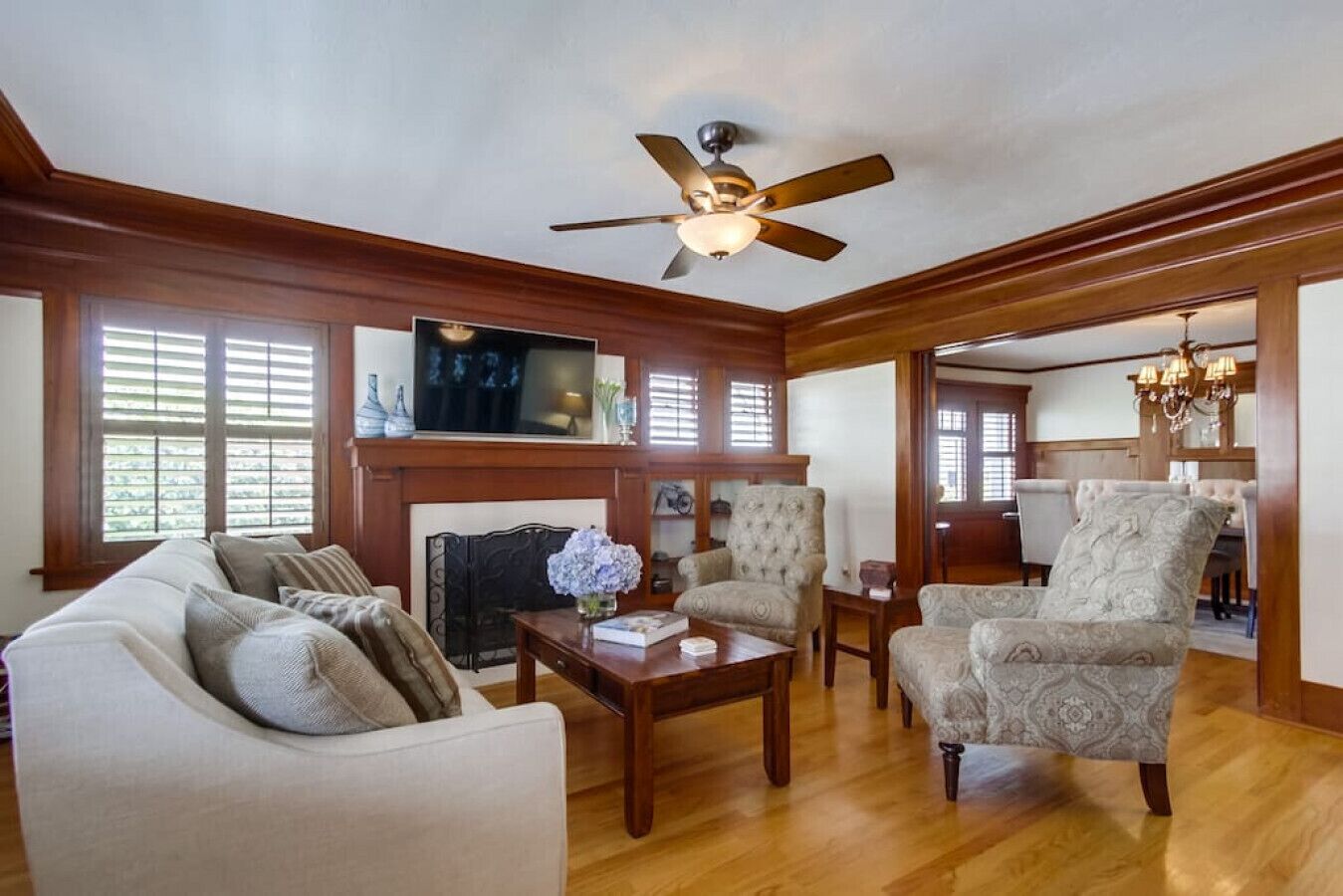 A spacious living room with a fireplace, a ceiling fan, and a dining area visible through an open doorway.