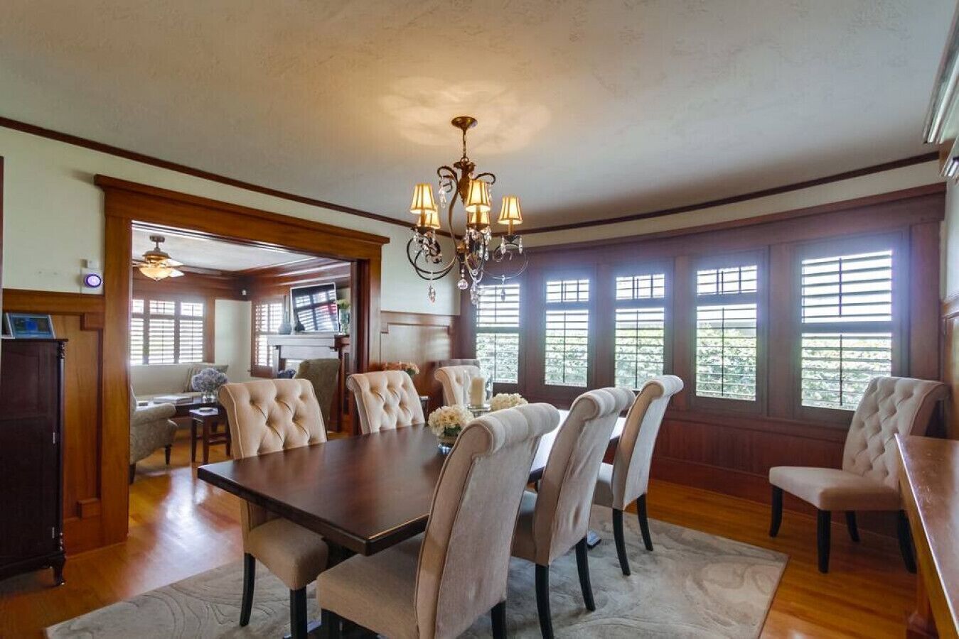 A dining room with a large wooden table, six upholstered chairs, and a chandelier.