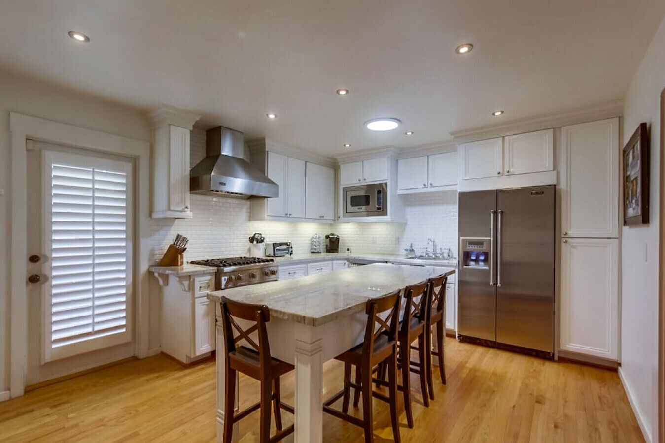 A spacious kitchen with white cabinetry, a central island with bar stools, a stainless steel refrigerator, and a microwave.