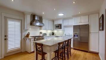 A spacious kitchen with white cabinetry, a central island with bar stools, a stainless steel refrigerator, and a microwave.