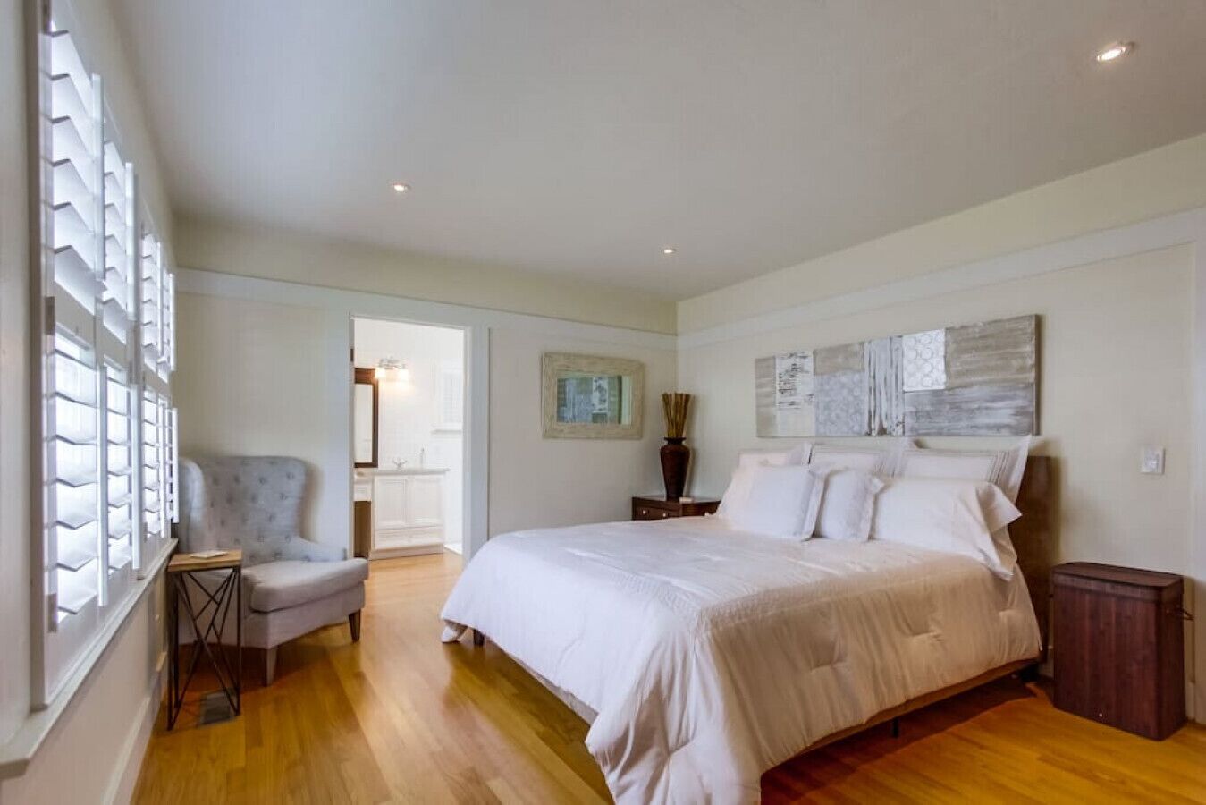 A bedroom with a large bed, a chair, a nightstand, and a window with blinds.