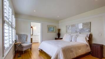 A bedroom with a large bed, a chair, a nightstand, and a window with blinds.