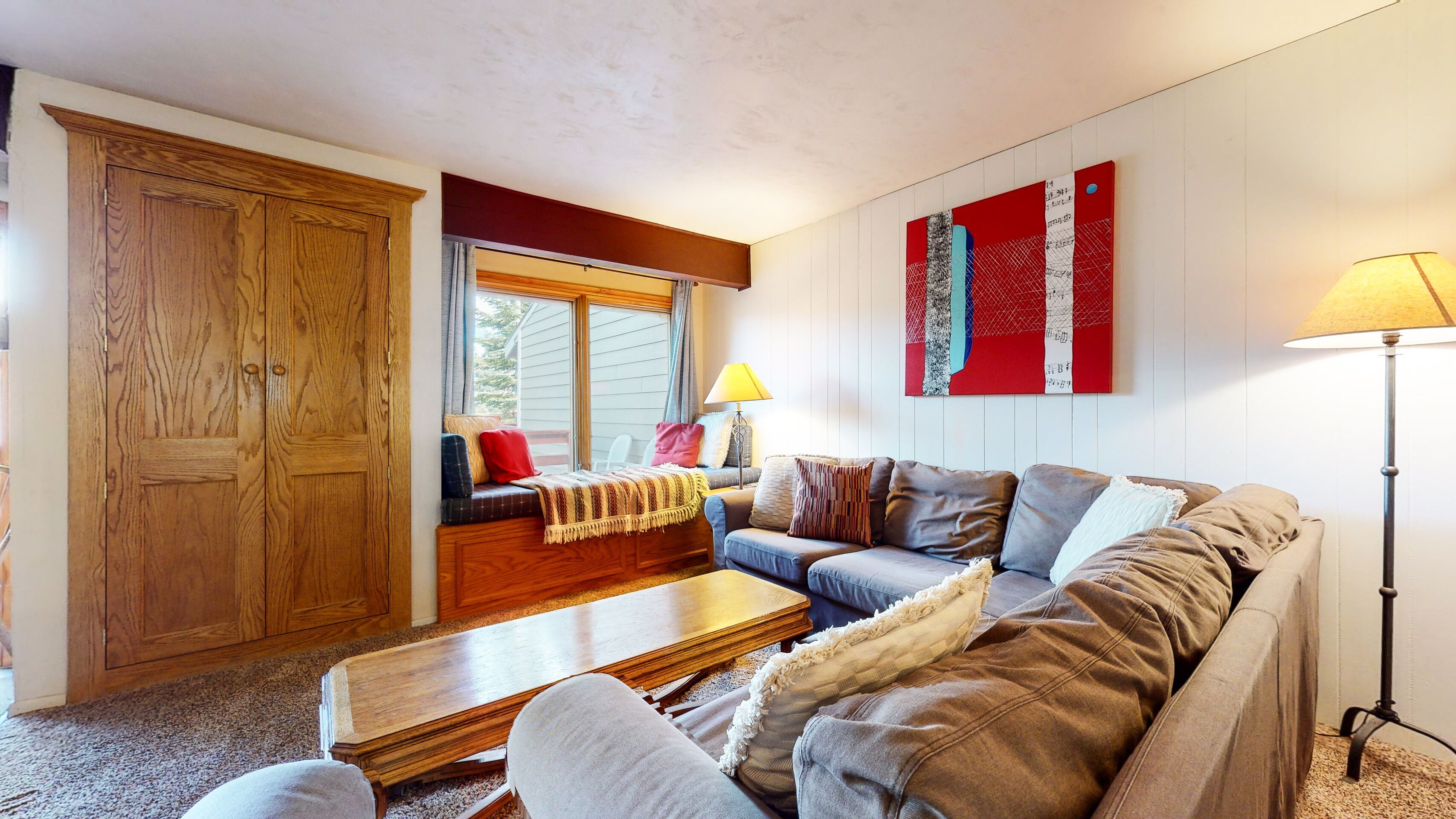 A cozy living room with a wooden wardrobe, a sofa, a coffee table, and a window with a view.