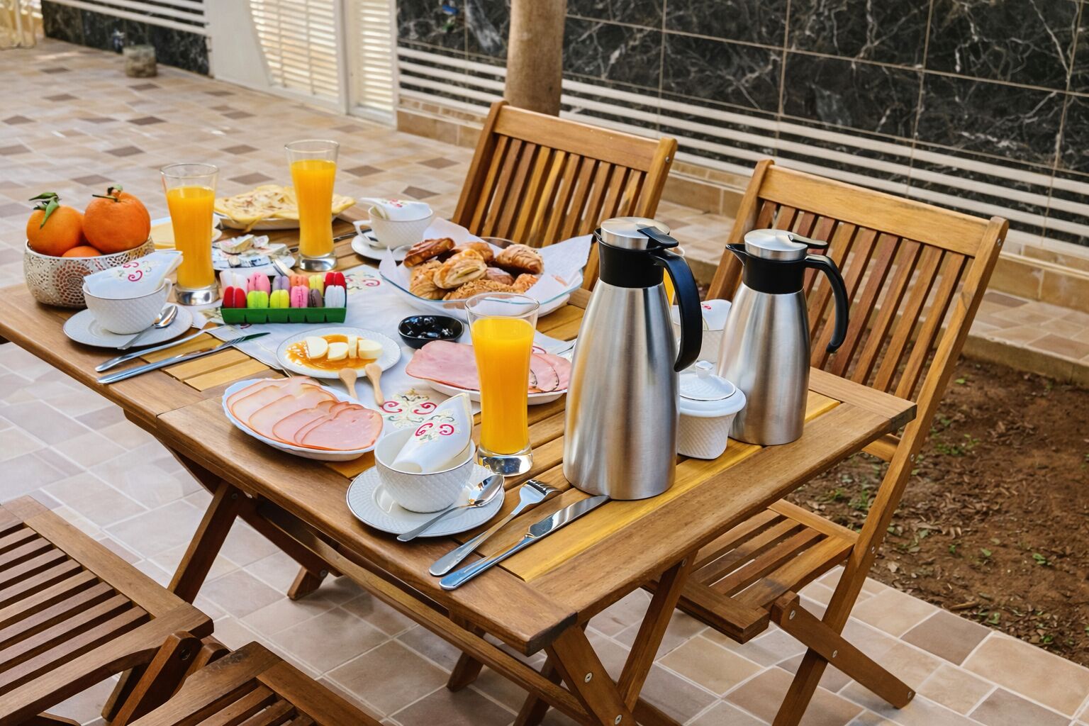 Een ontbijtsetting met een tafel, stoelen en diverse ontbijtartikelen, waaronder sinaasappelsap, gebak en koffie.