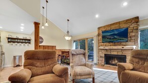 Una sala de estar con chimenea, dos sillones marrones, un tapete escocés y una pared de piedra con televisor.