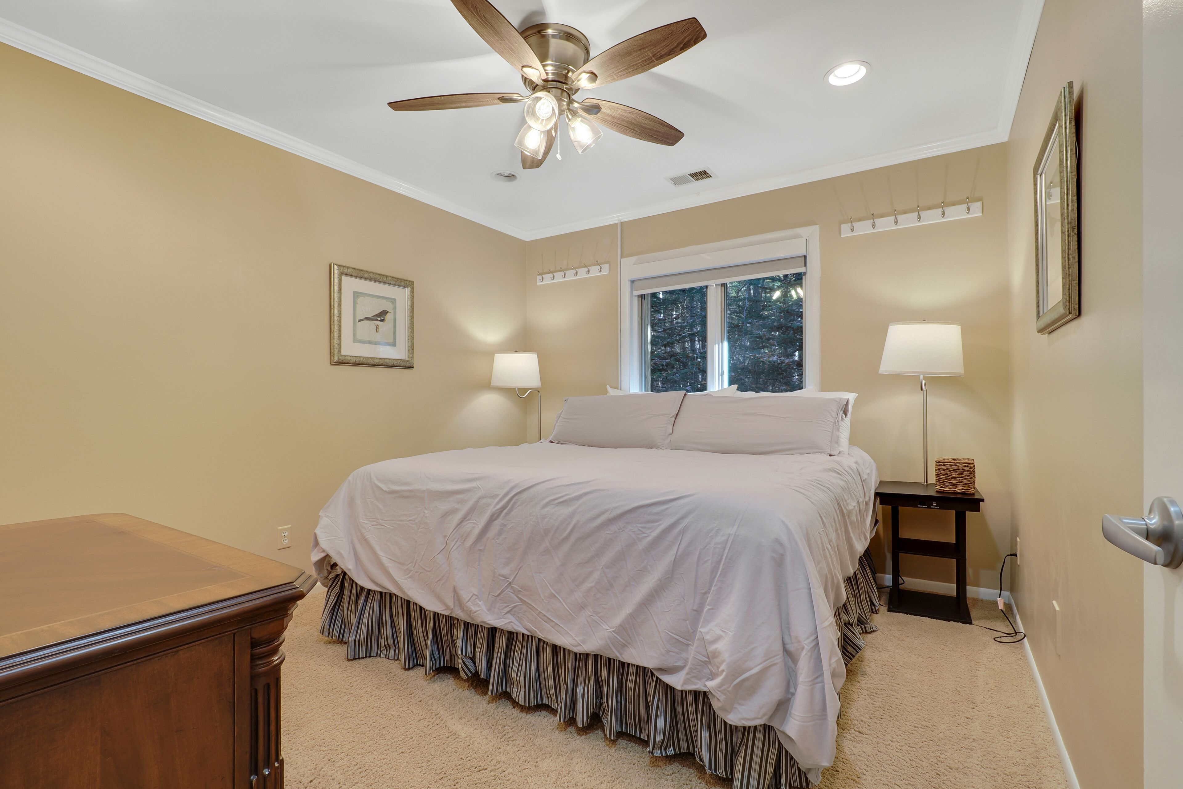 A bedroom with a bed, a ceiling fan, a window, and a nightstand with a lamp.