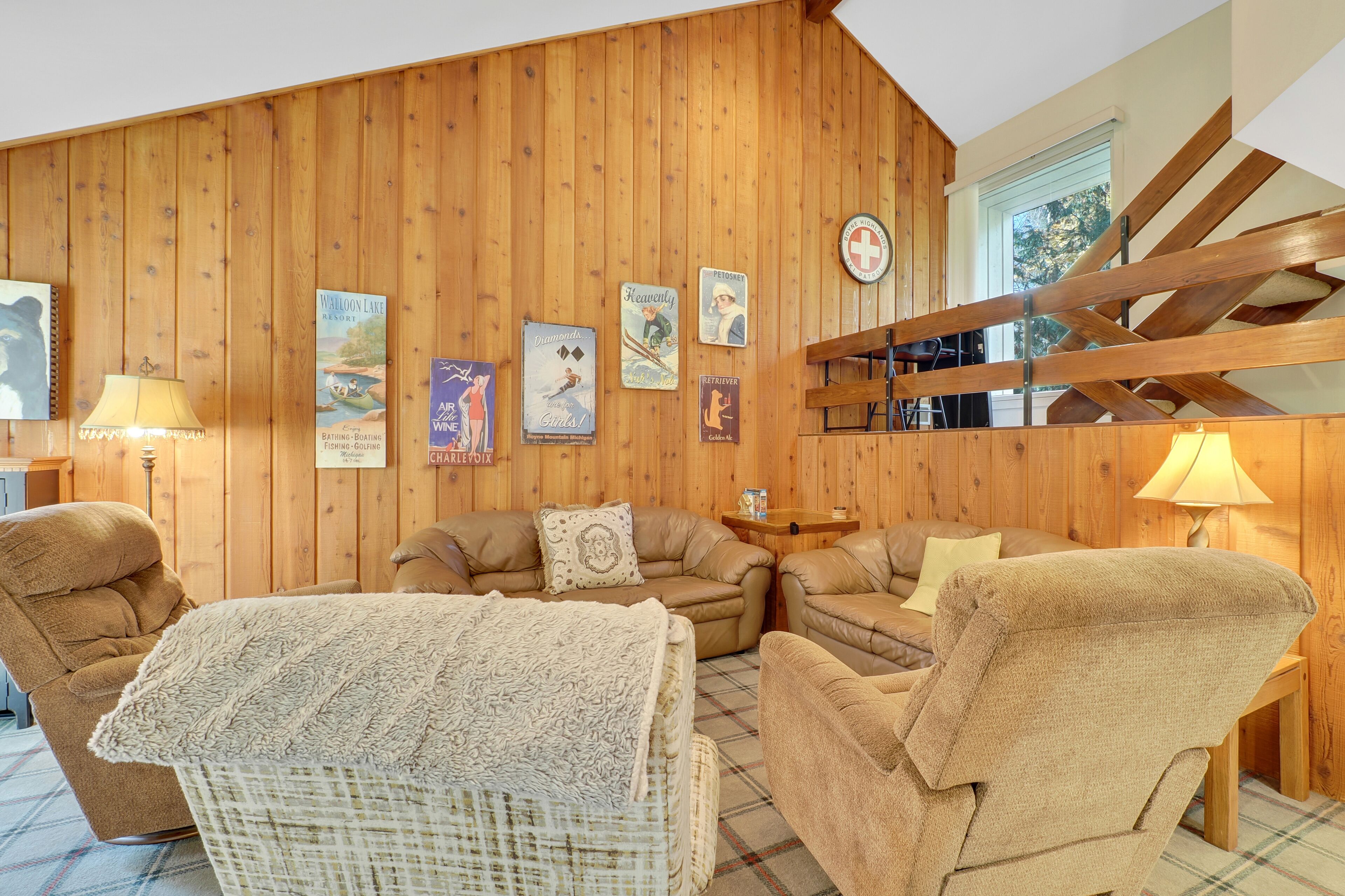 Una sala de estar acogedora con un muro de madera, un conjunto de sofás, una mesa de centro y una escalera.