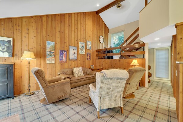 Une pièce chaleureuse avec des murs en bois, un sol à carreaux, un canapé, deux fauteuils, une lampe et une horloge.
