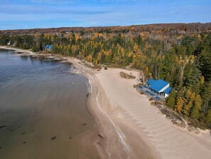 Une plage avec un bâtiment doté d’un toit bleu, entouré d’arbres aux feuilles d’automne.