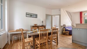 Un comedor con una mesa y sillas de madera, un radiador blanco, un cuadro en la pared y una escalera que sube a otra habitación.