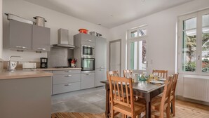Una cocina moderna con armarios grises, horno integrado y un comedor con sillas y mesa de madera.