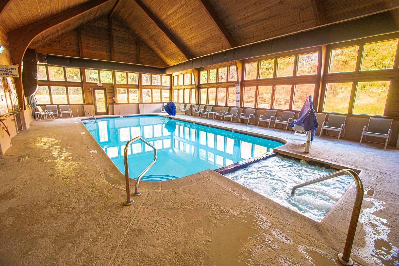 Piscina interior com teto de madeira e grandes janelas.