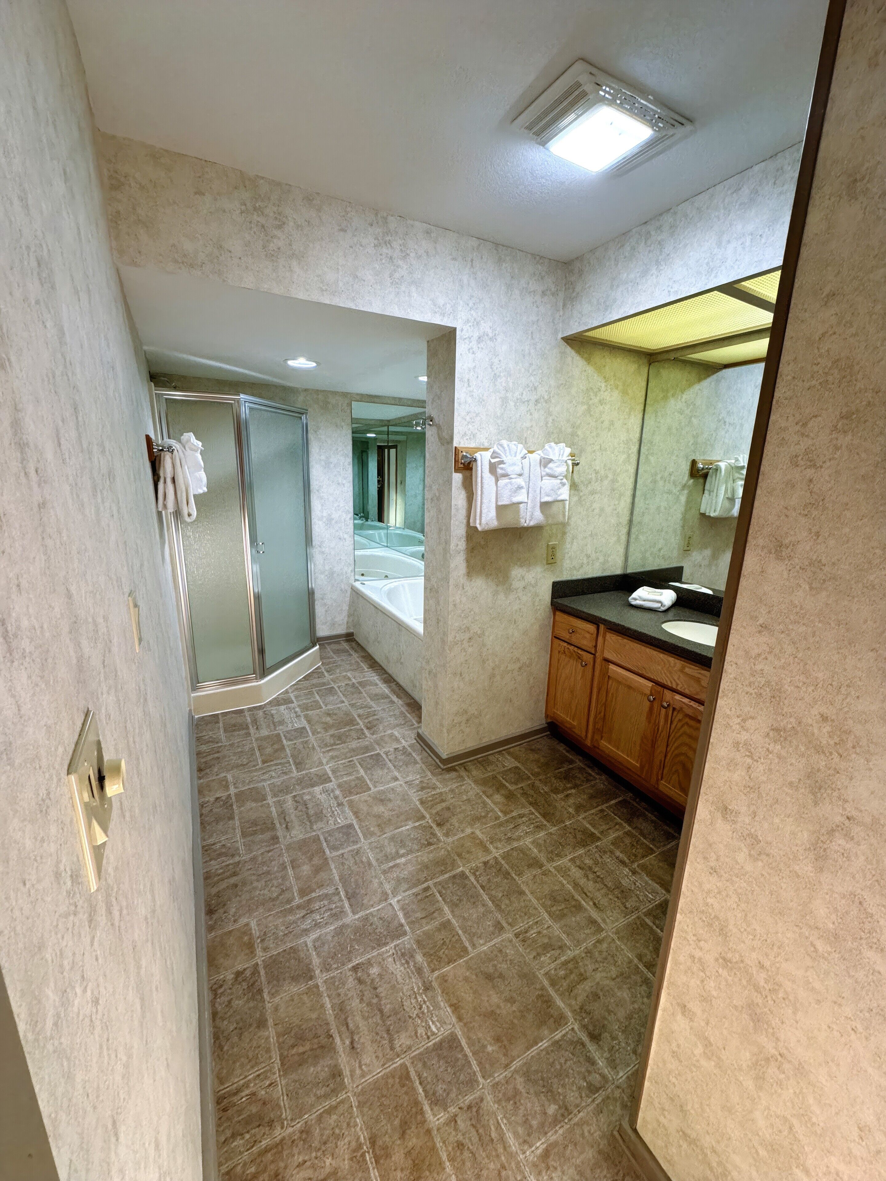 A bathroom with a glass shower enclosure, a sink with a mirror, and towels on a rack.
