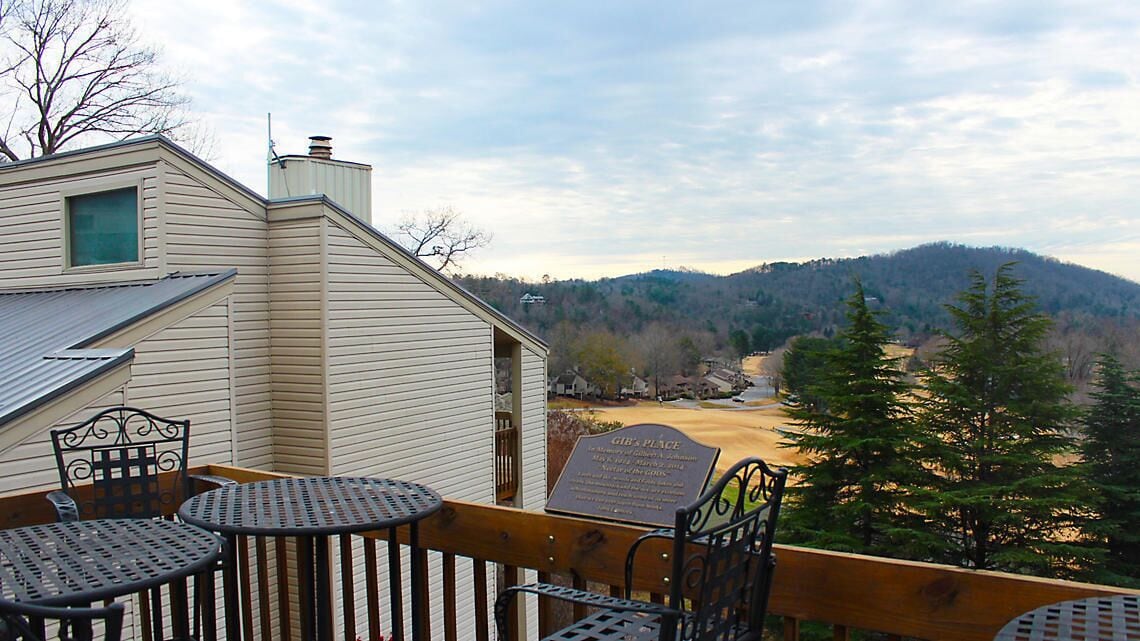 A balcony with metal chairs and a table, overlooking a hilly landscape with a building labeled "Gib's Place".