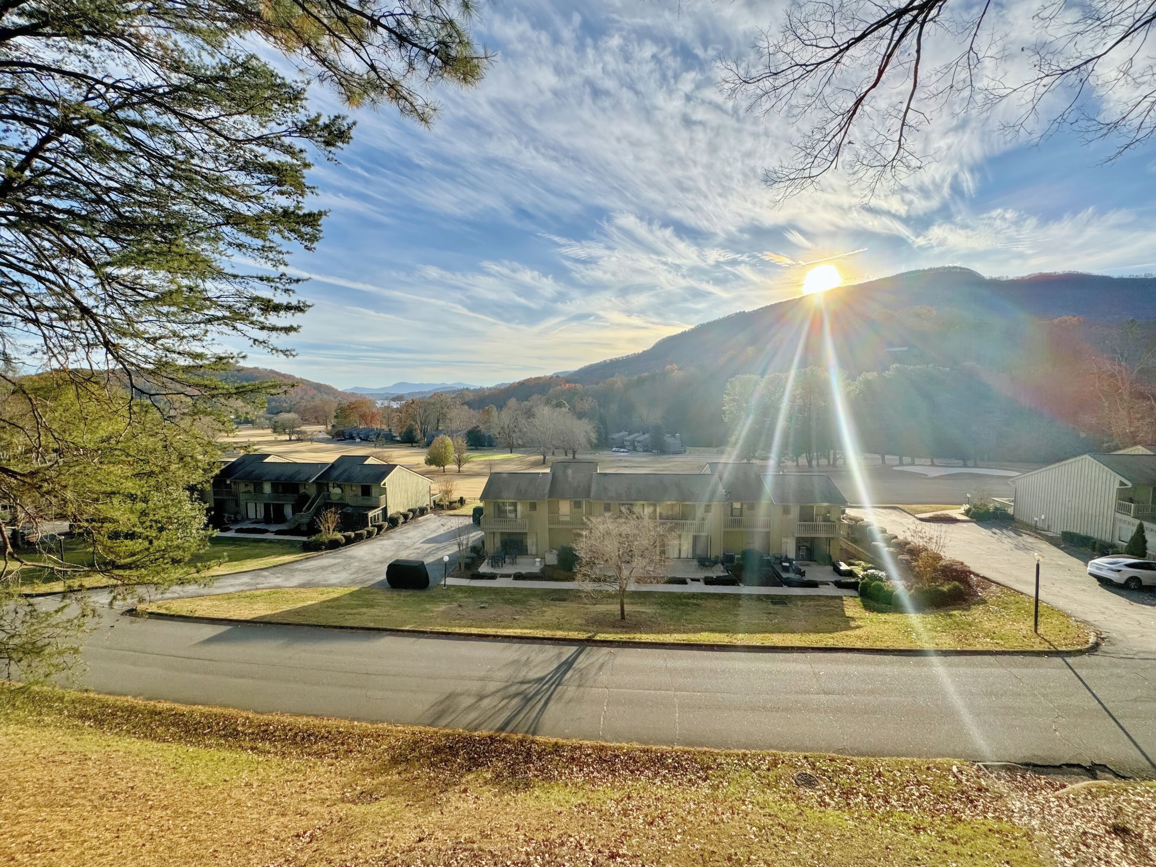 A residential area with houses and a large building, possibly a community center or clubhouse, surrounded by trees and hills in the background.