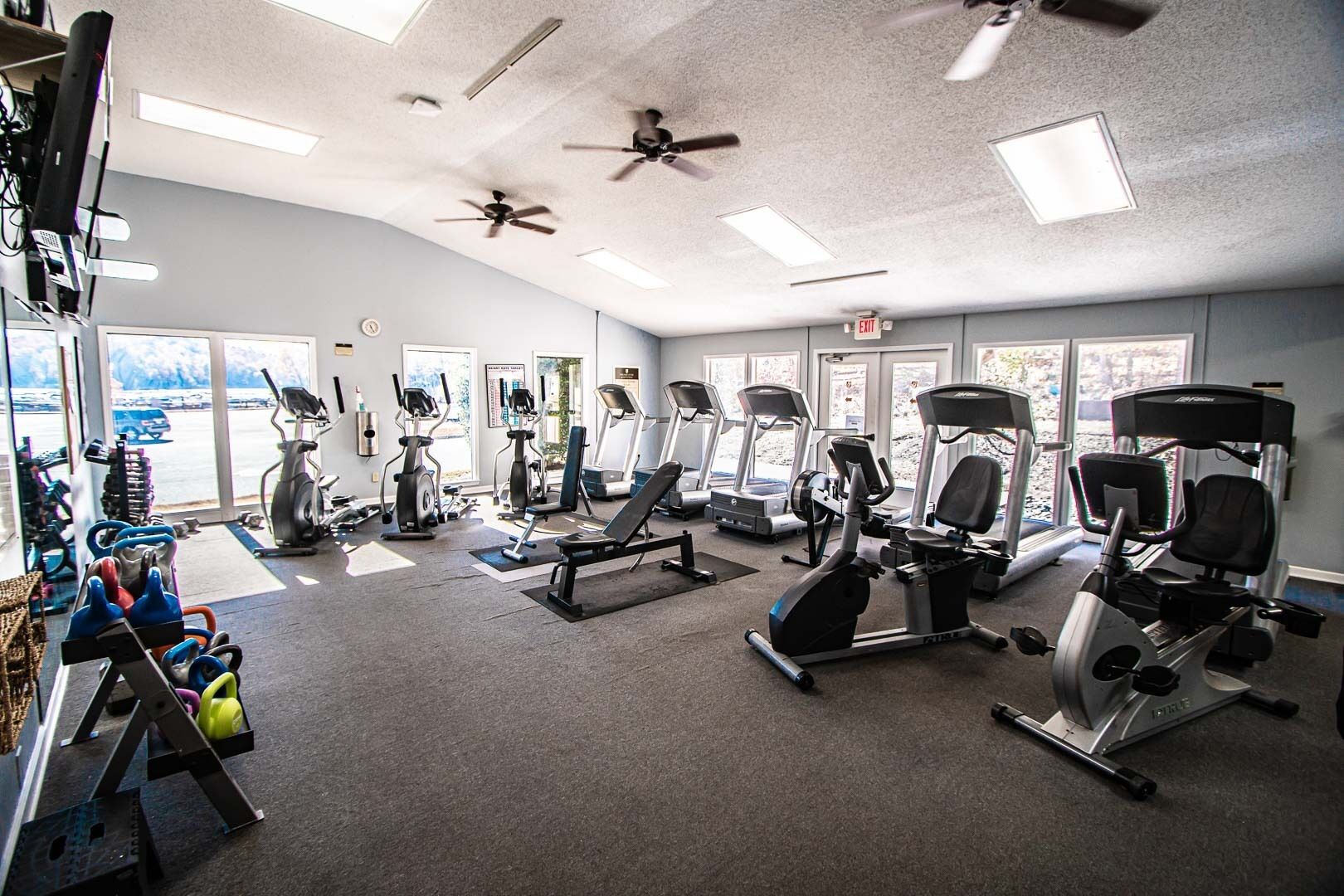 A gym with various exercise equipment, large windows, and ceiling fans.