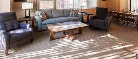 A living room with a sofa, two armchairs, a coffee table, and a dining area with a table and chairs.