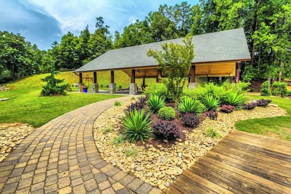 A covered outdoor area with a curved brick pathway leading to a building with a sloped roof.