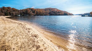 Una platja amb aigua cristal·lina, una riba sorrenca i un turó forestal al fons.