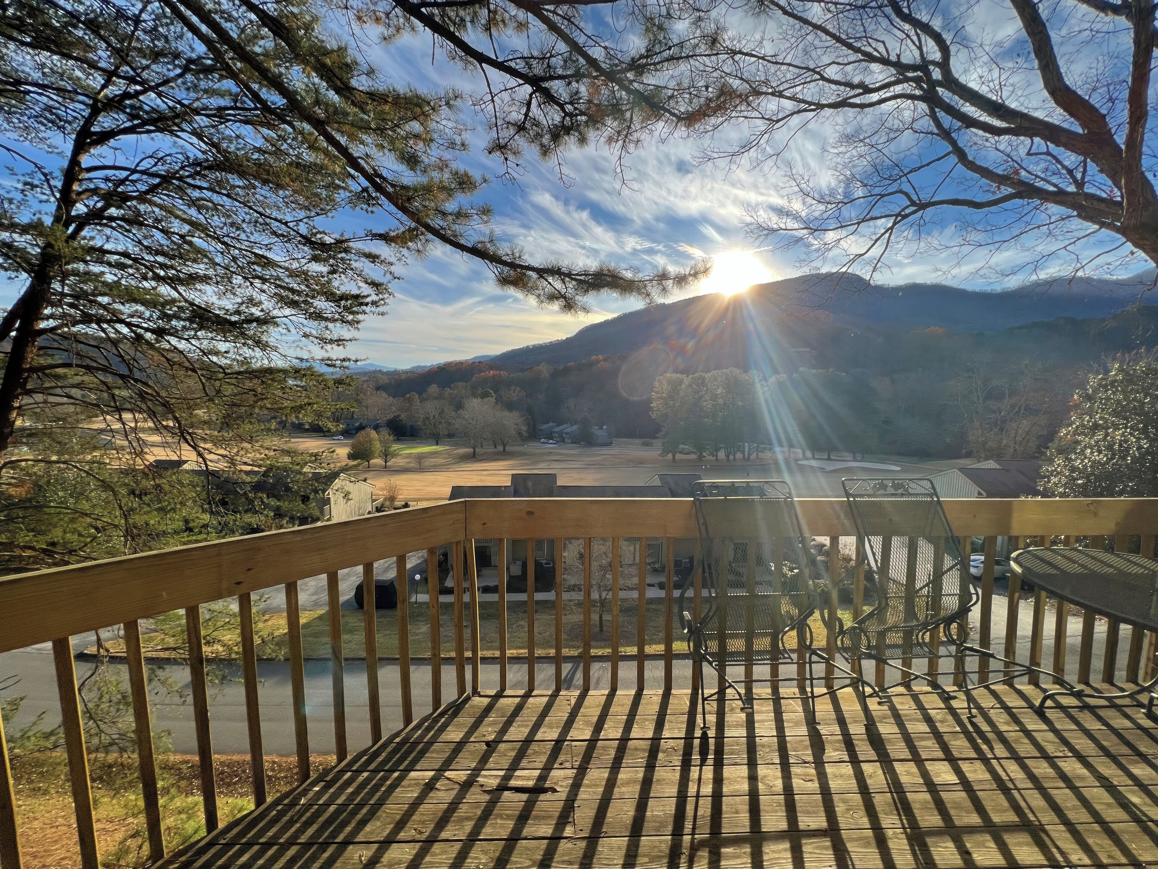 A wooden deck with metal chairs overlooking a river and a mountainous landscape.