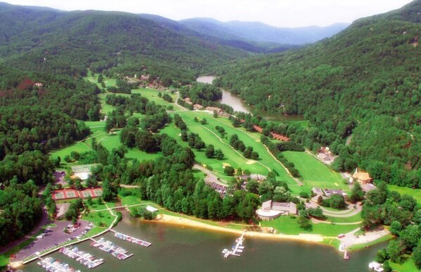 Vista aérea de un campo de golf con un lago, rodeado de colinas boscosas.