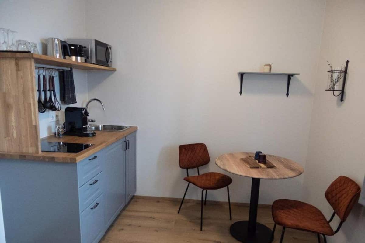 Eine kompakte Küche mit Mikrowelle, Toaster und Spüle, ein kleiner Esstisch mit vier Stühlen sowie ein Regal mit einer Tasse und einem dekorativen Gegenstand.