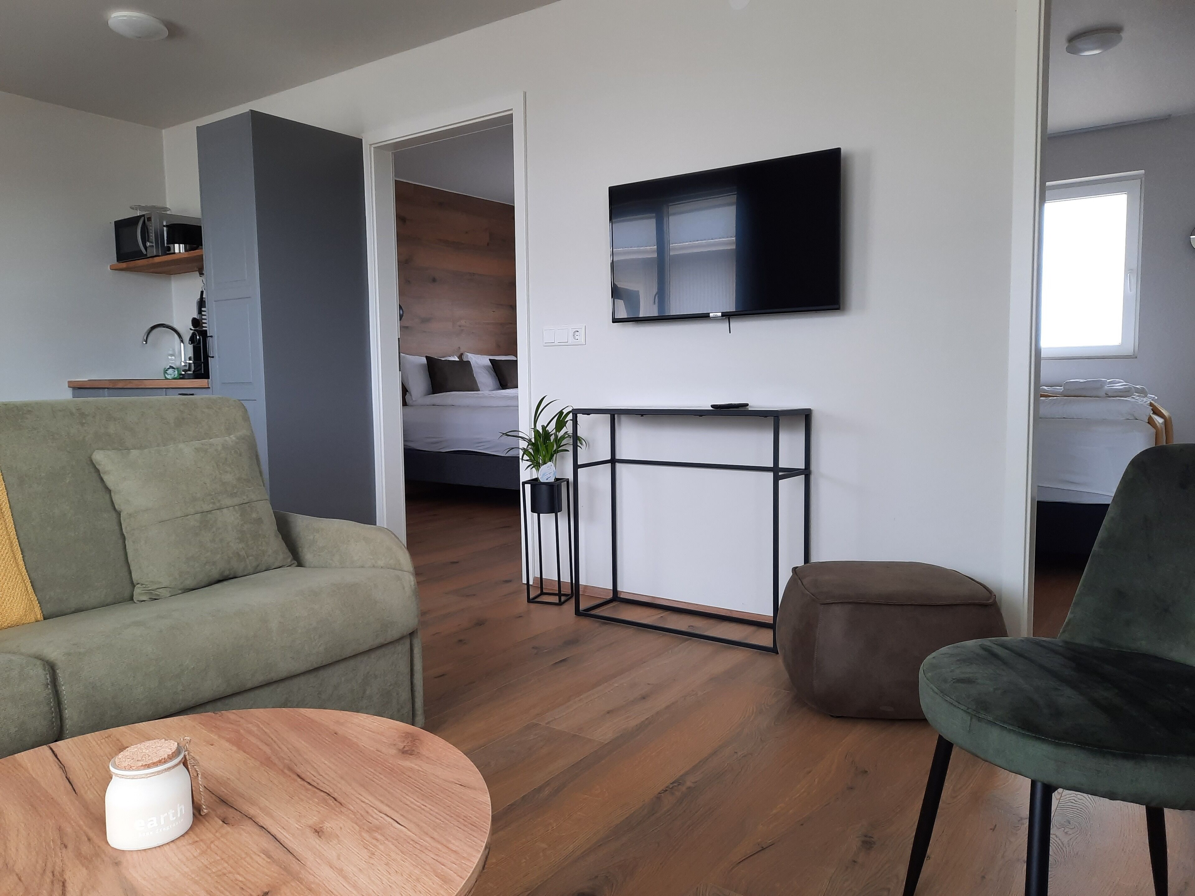 A modern living room with a sofa, a round wooden coffee table, a television mounted on the wall, and a small side table with a plant.