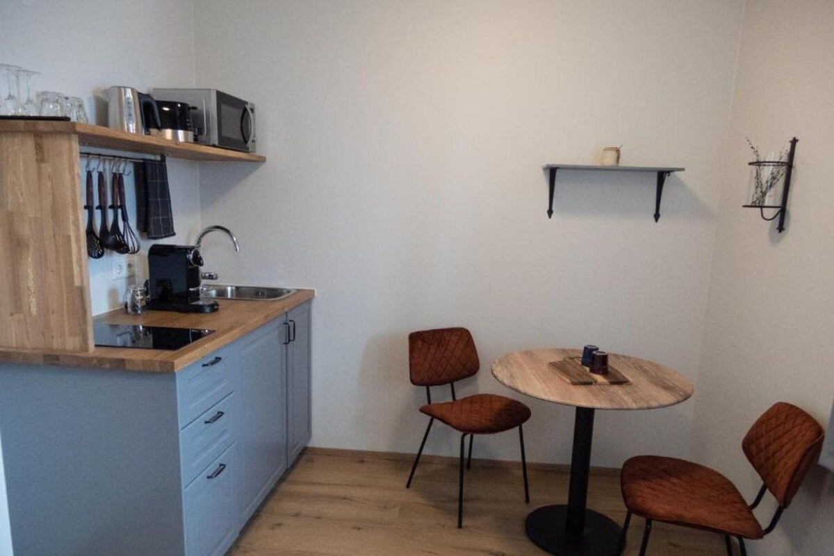 Une cuisine compacte équipée d’un four à micro-ondes, d’un grille-pain et d’un évier, ainsi qu’une petite table à manger avec des chaises et une étagère contenant des ustensiles de cuisine.