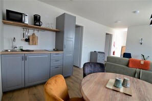 A modern kitchen with grey cabinets, a microwave, and a coffee maker. There is a dining area with a round table and two chairs.