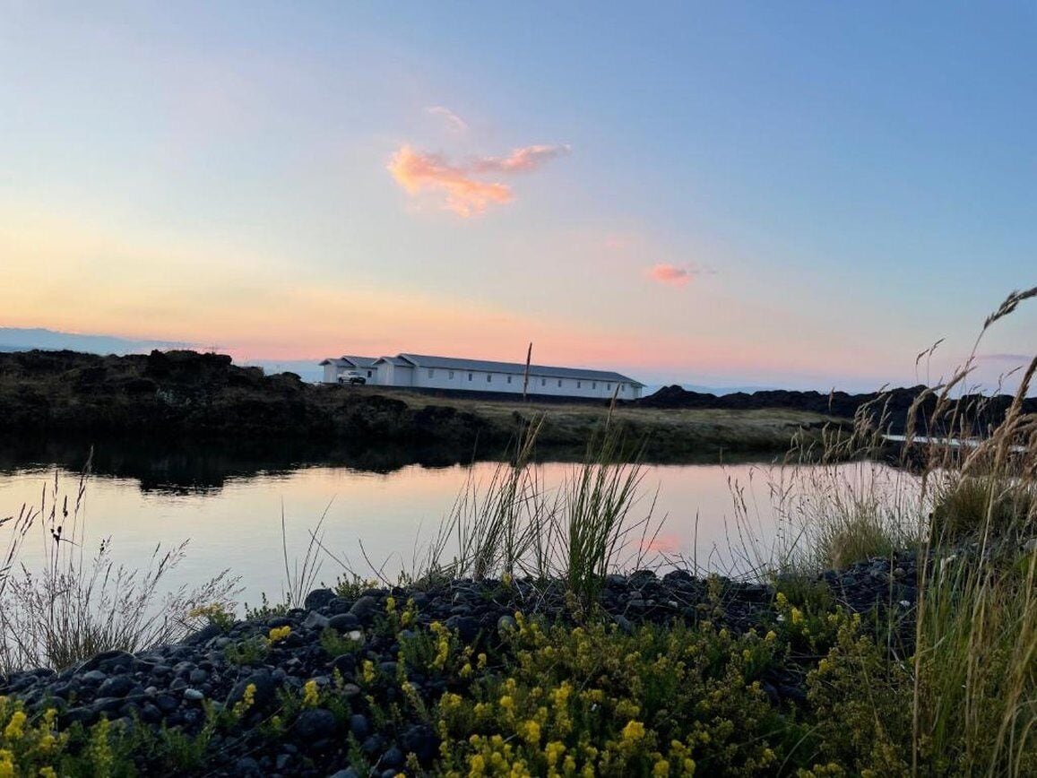 Un bâtiment blanc au bord d’une étendue d’eau calme, avec un ciel au coucher du soleil.