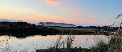 Un bâtiment blanc au bord d’une étendue d’eau calme, avec un ciel au coucher du soleil.