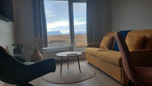 A living room with a sofa, chairs, a small table, and a view of a landscape through a window. - Stracta Apartments (Kirkjubaejarklaustur)
